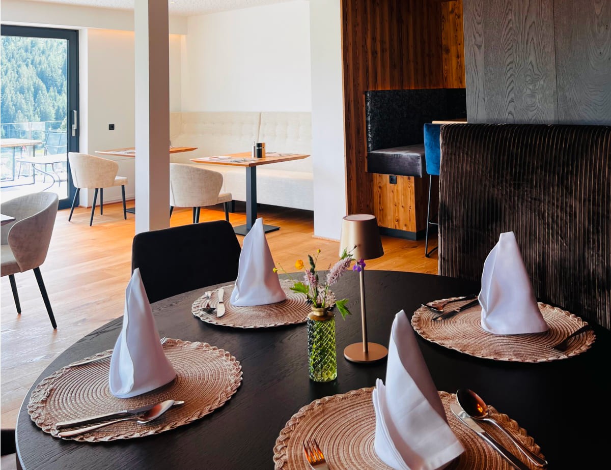 Elegantes Restaurant im Landhaus Ramsau mit gedecktem Tisch und Blick auf Wald durch große Fenster