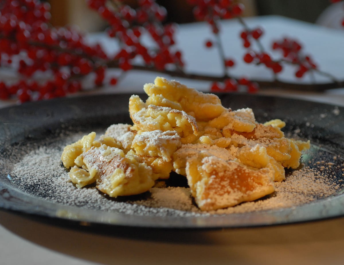 Kaiserschmarrn auf einem Teller mit Puderzucker bestäubt, im Hintergrund rote Beeren